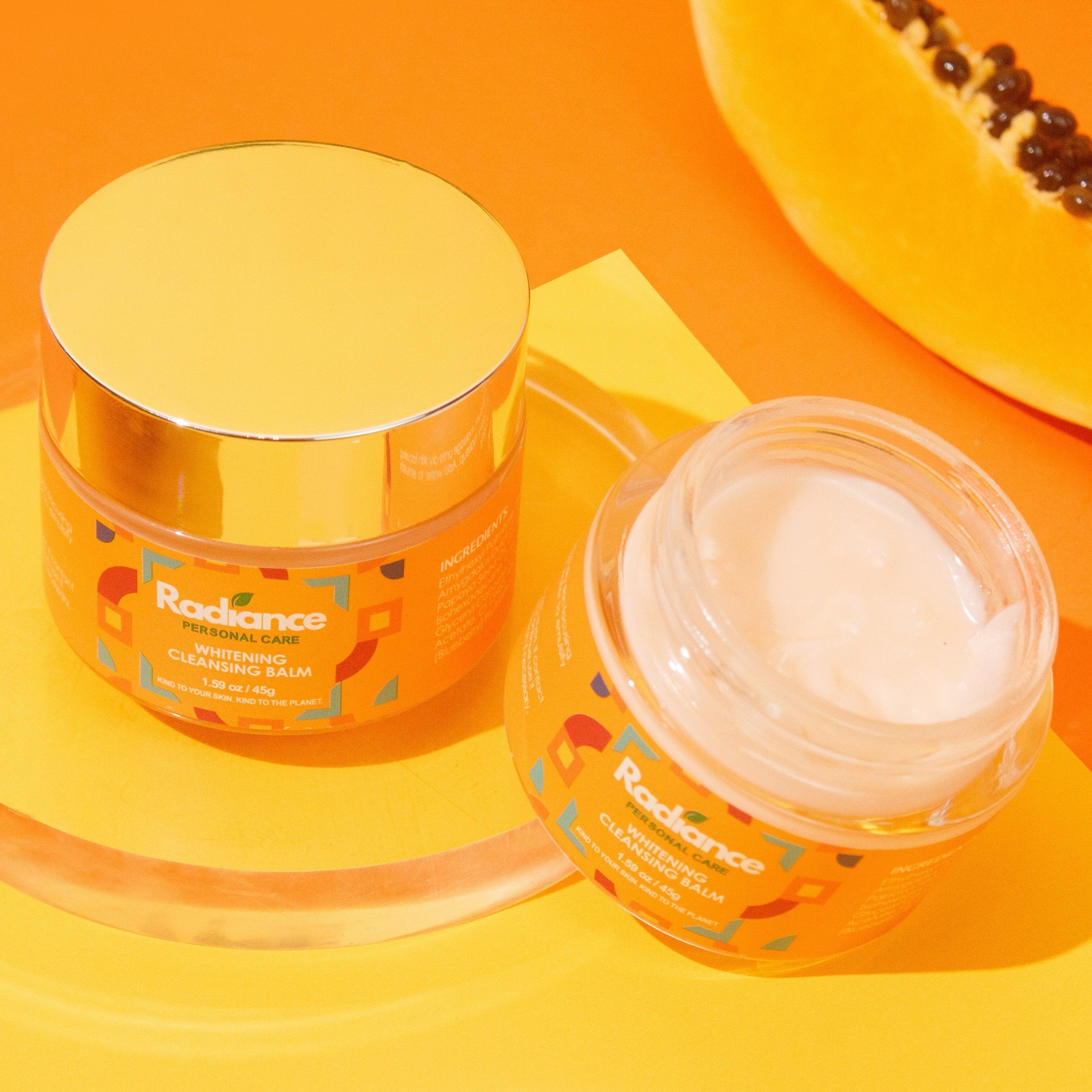Two jars of Radiance skincare product on an orange background with a halved papaya.